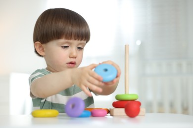 Photo of Cute little child playing with toy pyramid at table indoors