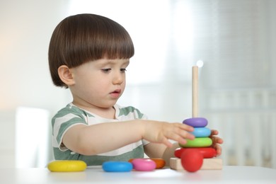 Photo of Cute little child playing with toy pyramid at table indoors