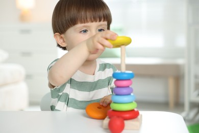 Photo of Cute little child playing with toy pyramid at table indoors