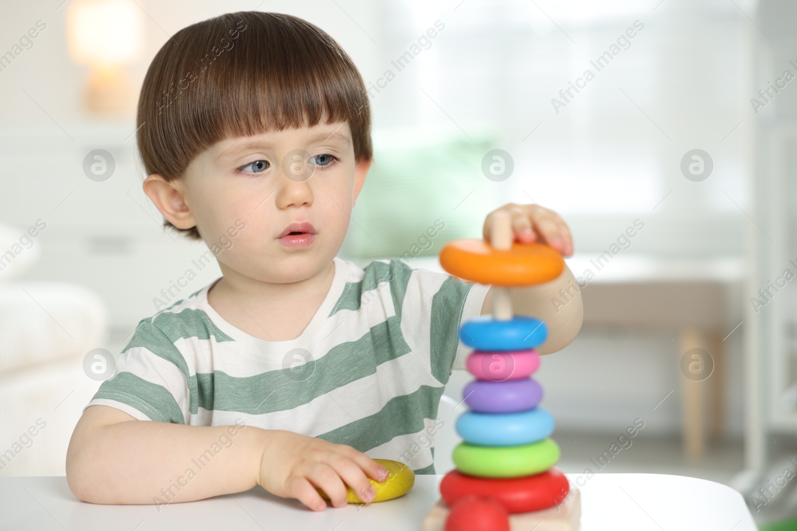Cute little child playing with toy pyramid at table indoors Photo of Cute little child playing with toy pyramid at table indoors