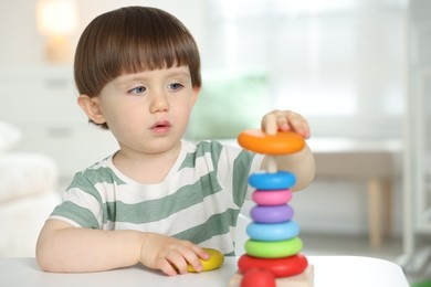 Photo of Cute little child playing with toy pyramid at table indoors