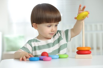Photo of Cute little child playing with toy pyramid at table indoors