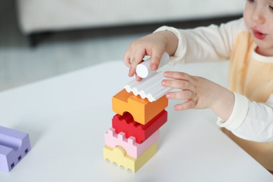 Photo of Cute little child playing with building bricks at white table indoors, closeup
