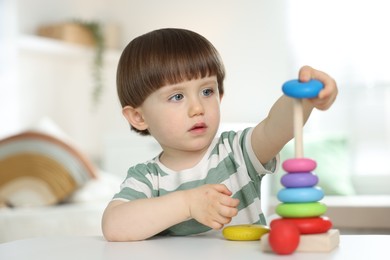 Photo of Cute little child playing with toy pyramid at table indoors
