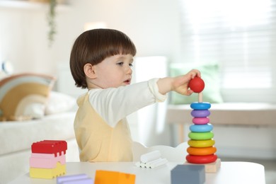 Photo of Cute little child playing with toy pyramid at table indoors
