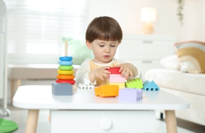 Photo of Cute little child playing with toys at table indoors