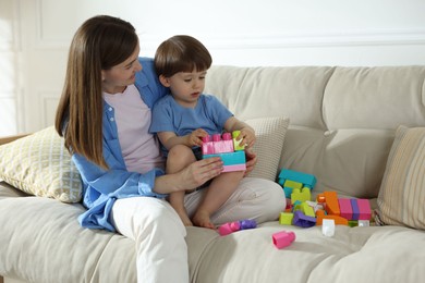 Photo of Mother and son playing with building bricks on sofa at home