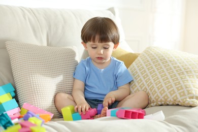 Photo of Cute little child playing with building bricks on sofa at home