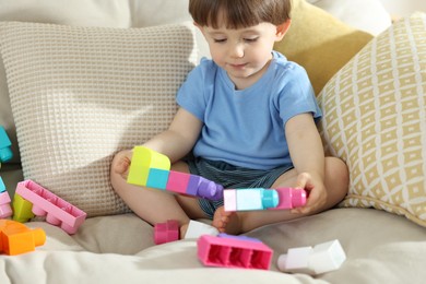 Photo of Cute little child playing with building bricks on sofa at home