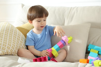 Photo of Cute little child playing with building bricks on sofa at home