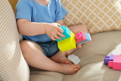 Photo of Cute little child playing with building bricks on sofa at home, closeup