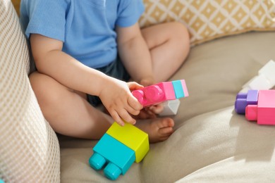 Photo of Cute little child playing with building bricks on sofa at home, closeup