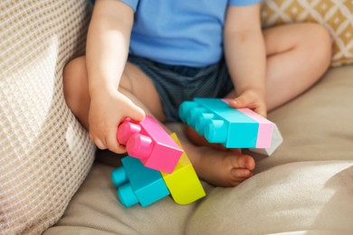 Photo of Cute little child playing with building bricks on sofa at home, closeup