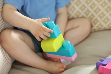Photo of Cute little child playing with building bricks on sofa at home, closeup