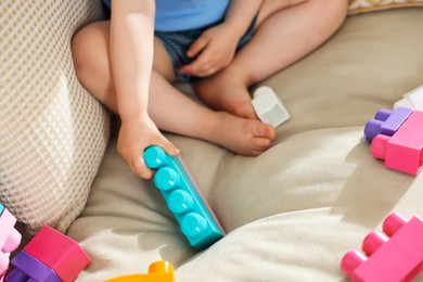 Photo of Cute little child playing with building bricks on sofa at home, closeup