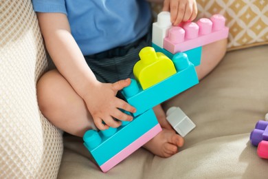 Photo of Cute little child playing with building bricks on sofa at home, closeup
