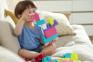 Photo of Cute little child playing with building bricks on sofa at home