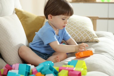 Photo of Cute little child playing with building bricks on sofa at home