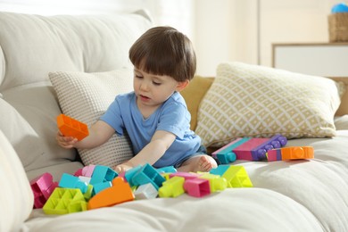Photo of Cute little child playing with building bricks on sofa at home