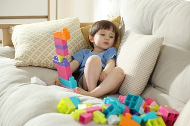 Photo of Cute little child playing with building bricks on sofa at home