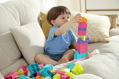 Photo of Cute little child playing with building bricks on sofa at home