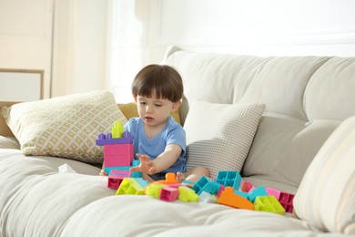 Photo of Cute little child playing with building bricks on sofa at home