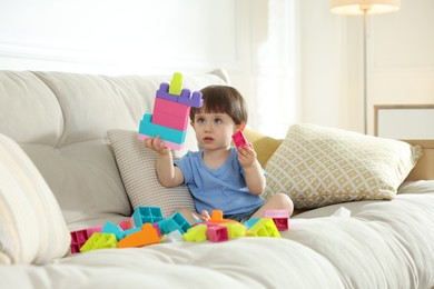 Photo of Cute little child playing with building bricks on sofa at home
