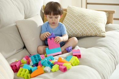 Photo of Cute little child playing with building bricks on sofa at home