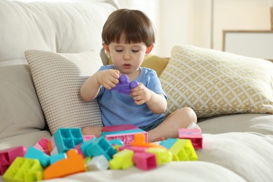 Photo of Cute little child playing with building bricks on sofa at home