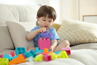 Photo of Cute little child playing with building bricks on sofa at home