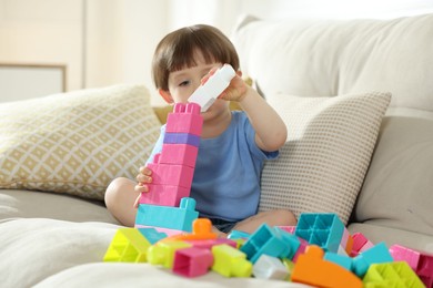 Photo of Cute little child playing with building bricks on sofa at home