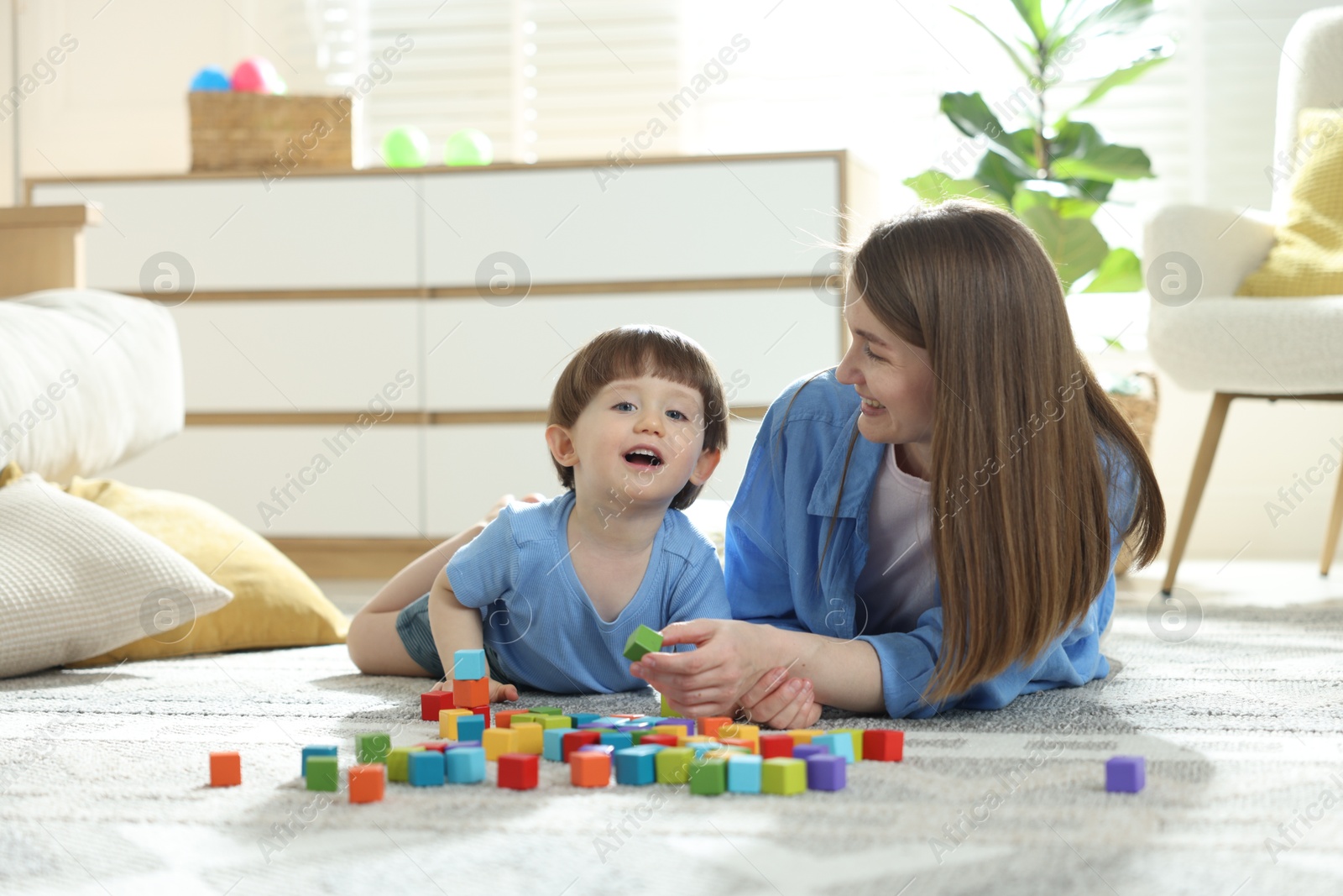 Photo of Mother and son playing with colorful cubes at home. Space for text