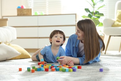 Photo of Mother and son playing with colorful cubes at home. Space for text