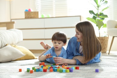 Photo of Mother and son playing with colorful cubes at home. Space for text