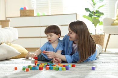 Photo of Mother and son playing with colorful cubes at home. Space for text