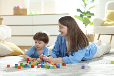 Photo of Mother and son playing with colorful cubes at home. Space for text