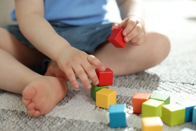 Photo of Cute little child playing with colorful cubes at home, closeup