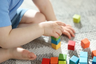 Photo of Cute little child playing with colorful cubes at home, closeup