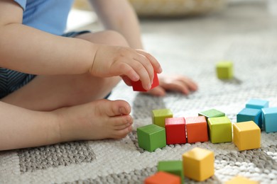 Photo of Cute little child playing with colorful cubes at home, closeup
