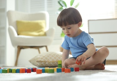 Photo of Cute little child playing with colorful cubes at home