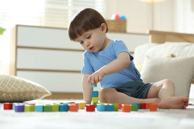 Photo of Cute little child playing with colorful cubes at home