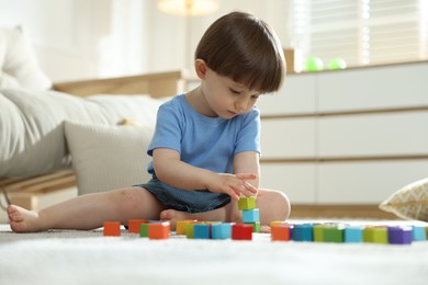 Photo of Cute little child playing with colorful cubes at home