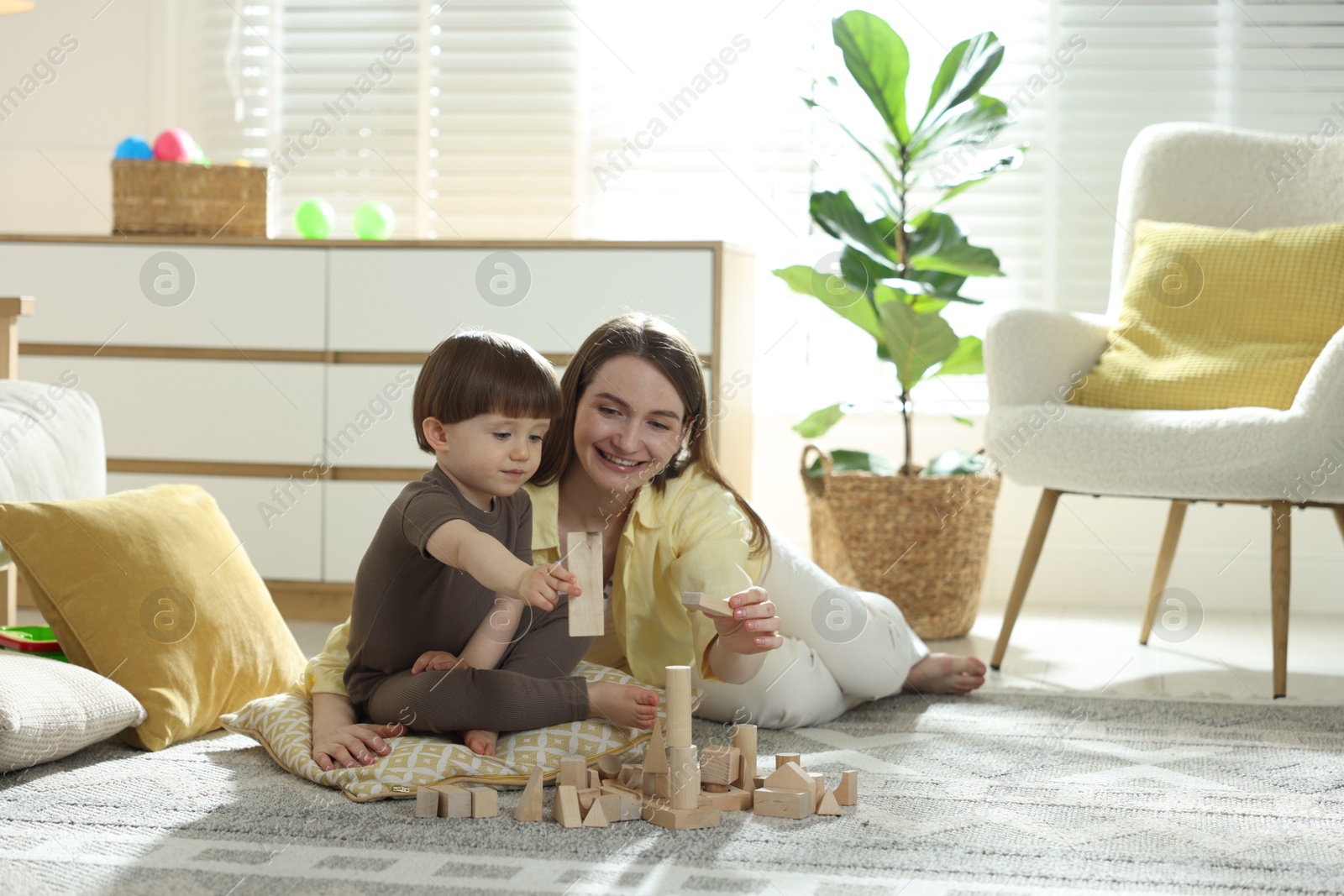 Photo of Mother and son playing with wooden building blocks at home. Space for text