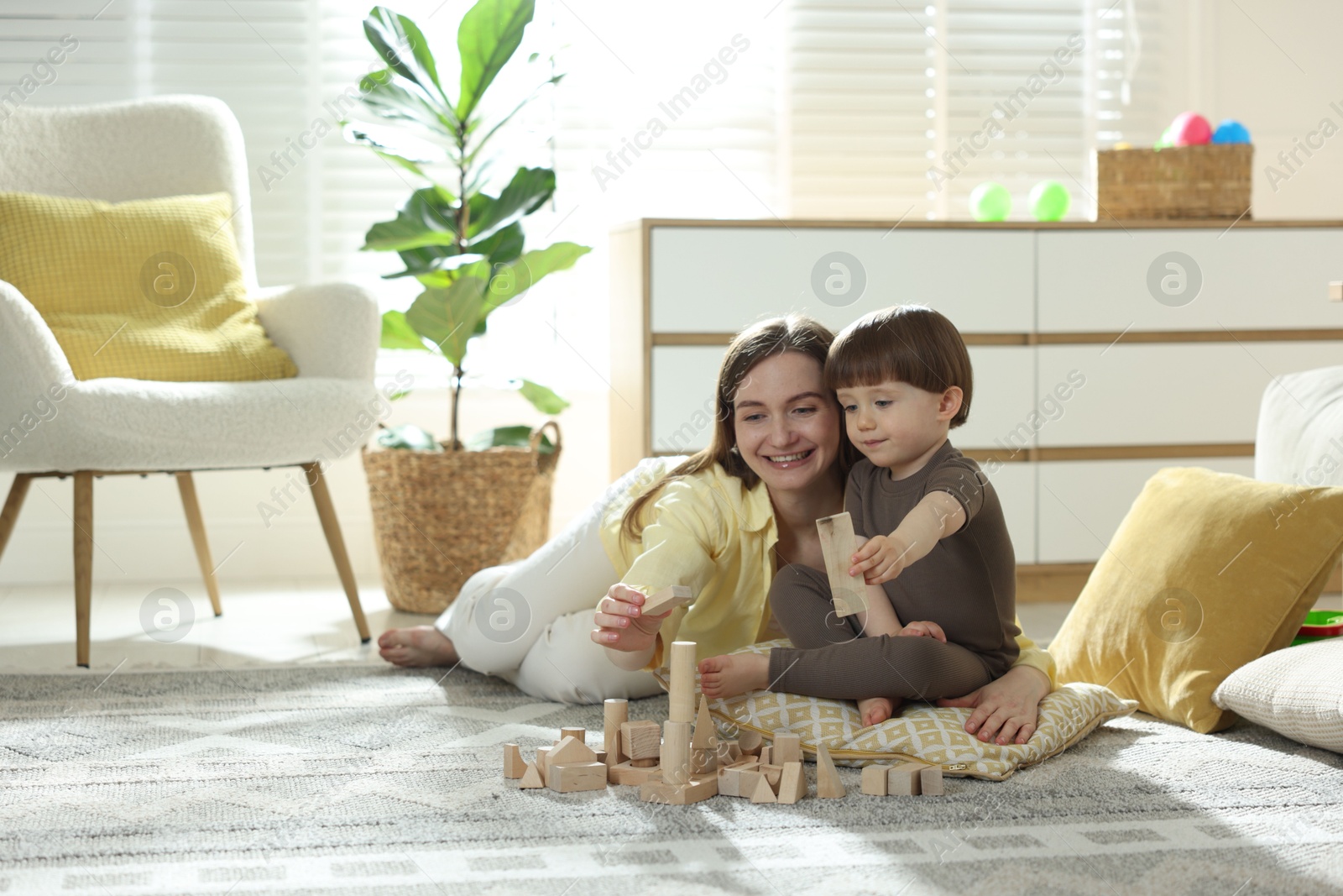 Photo of Mother and son playing with wooden building blocks at home. Space for text
