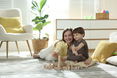 Photo of Mother and son playing with wooden building blocks at home. Space for text