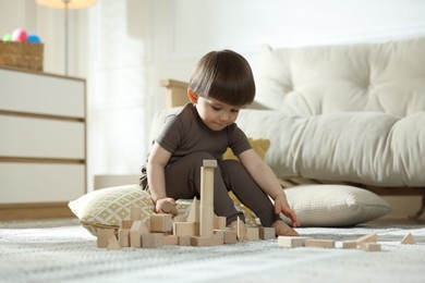 Photo of Cute little child playing with wooden building blocks at home