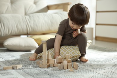 Photo of Cute little child playing with wooden building blocks at home