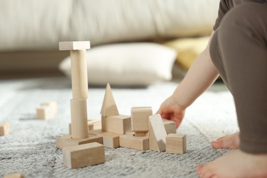 Photo of Cute little child playing with wooden building blocks at home, closeup