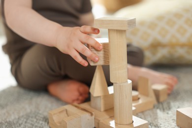Photo of Cute little child playing with wooden building blocks at home, closeup