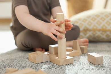 Photo of Cute little child playing with wooden building blocks at home, closeup